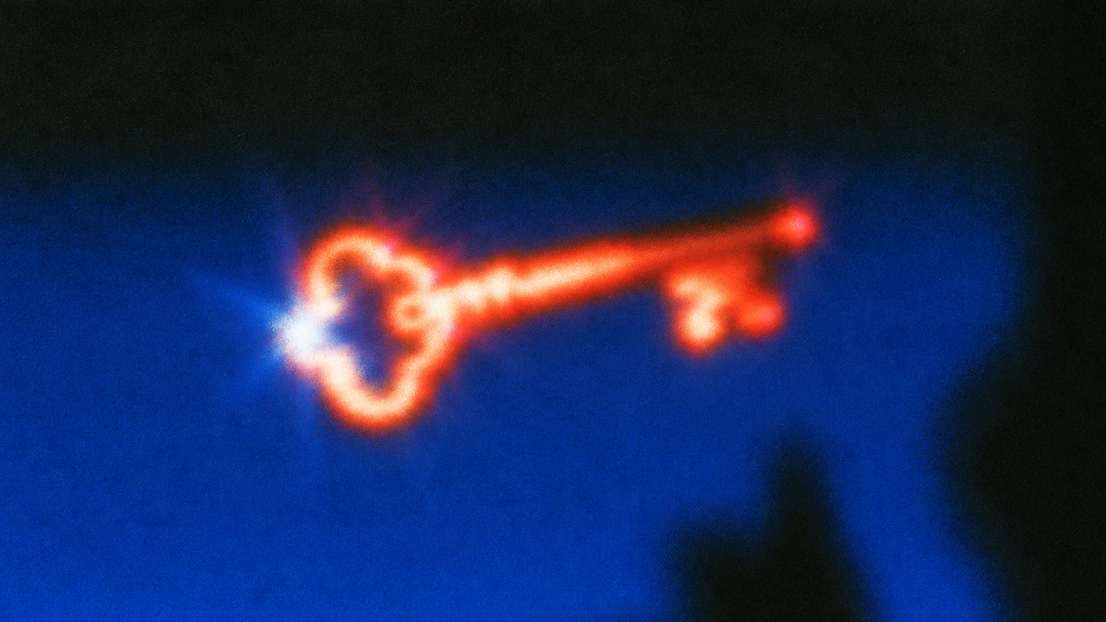 Grainy film still of a glowing orange skeleton key floating in deep cobalt blue