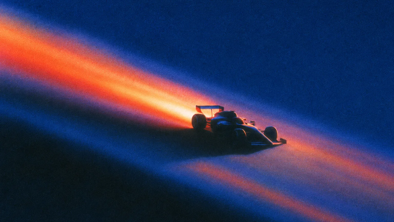 Grainy night scene of a dark Formula 1 car speeding diagonally across a deep blue frame, trailing a blazing orange streak of light