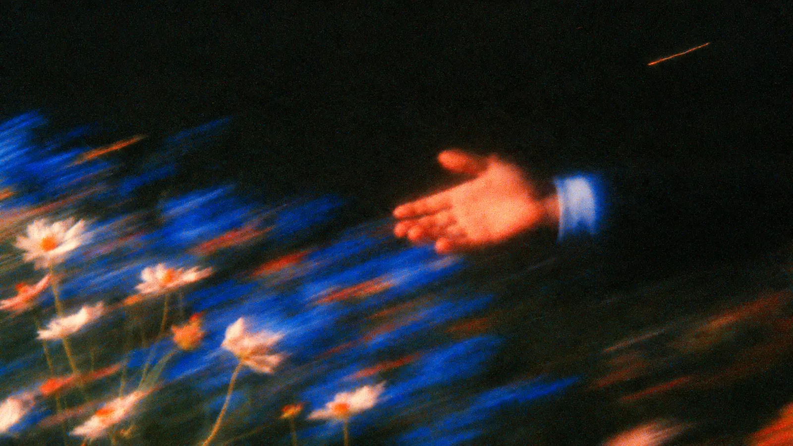 Motion-blurred film still of an open hand in a blue cuff reaching over white daisies and cobalt flowers in the dark